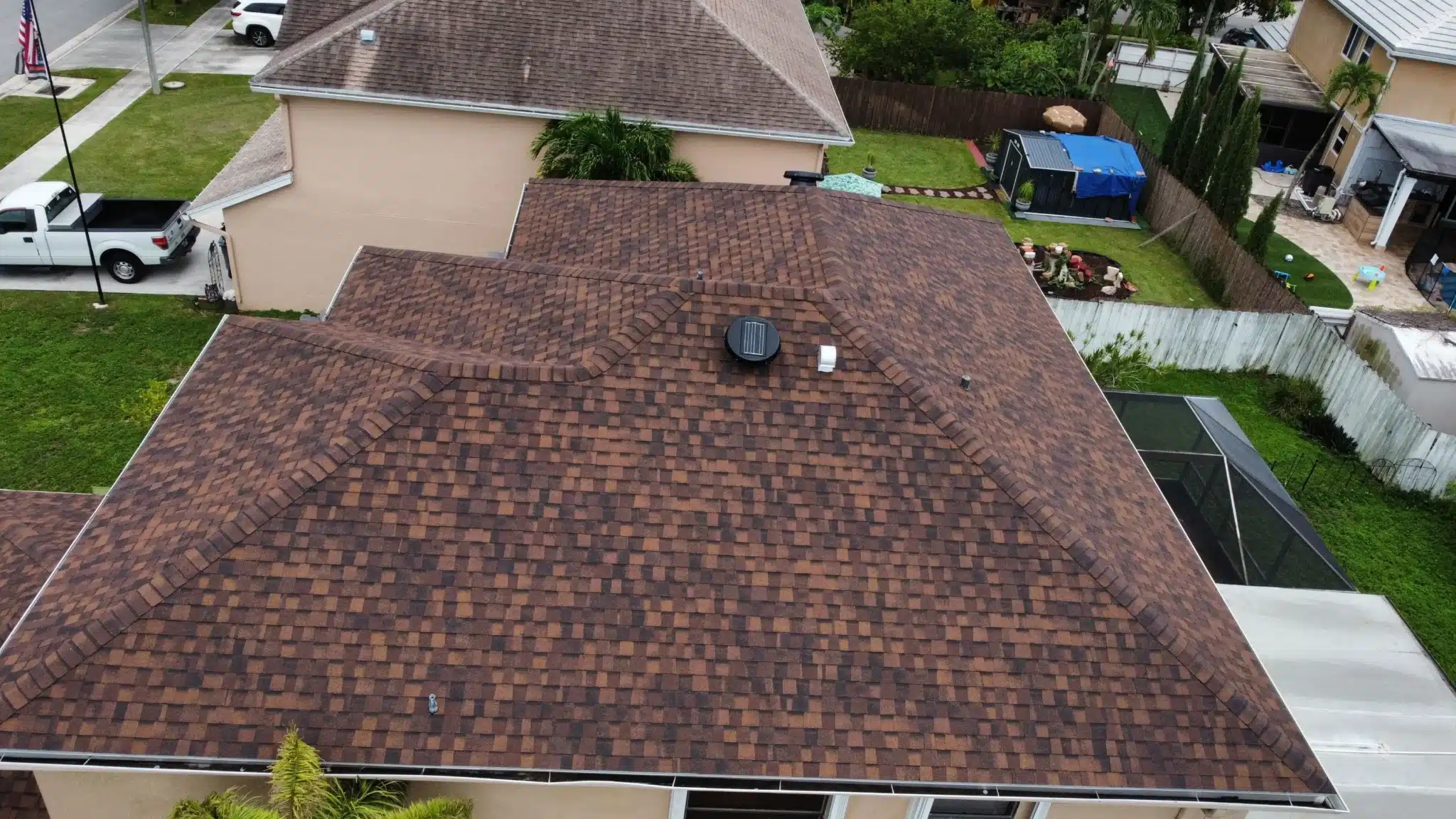 Aerial view of a well-maintained residential roof in Hollywood, FL, featuring brown shingles and a solar vent, highlighting expert roof repair services by Dream Team Roofing.