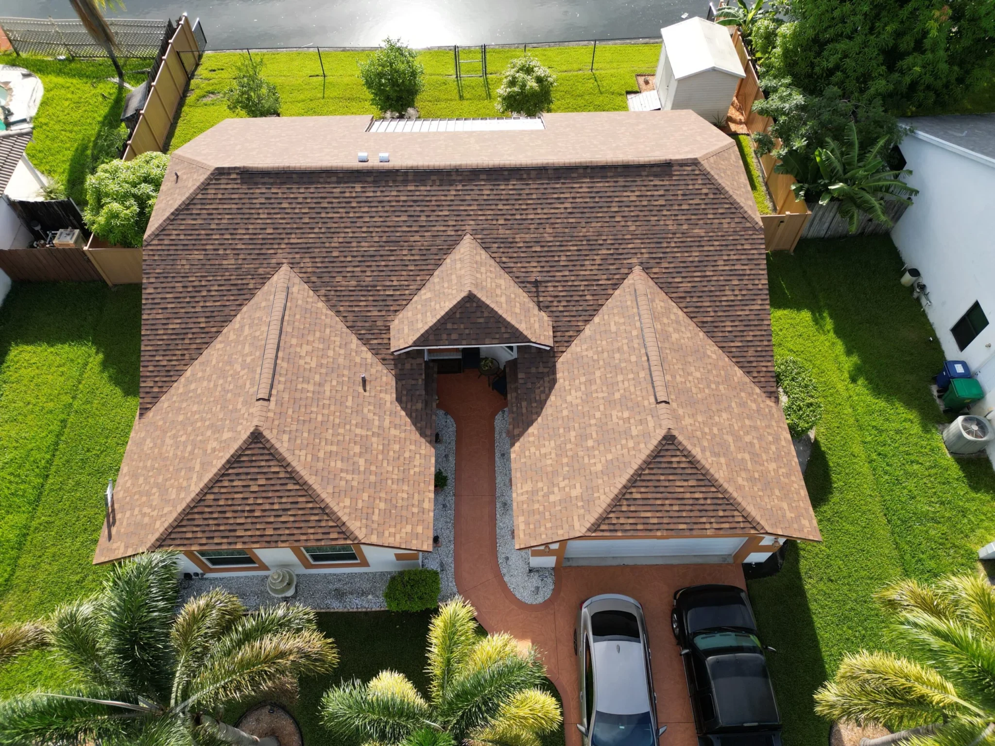 Aerial view of a residential home in Plantation, Florida, showcasing a newly installed asphalt shingle roof with a brown color scheme, surrounded by green grass and palm trees, highlighting Dream Team Roofing's quality roof repair services.